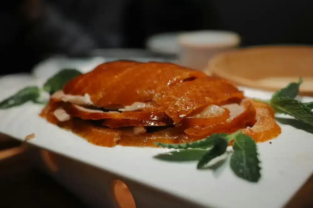 Sliced crispy Peking duck with mint leaves on a white plate
